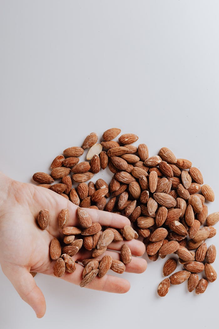 creative A hand holding raw almonds on a white background, showcasing healthy snack options.